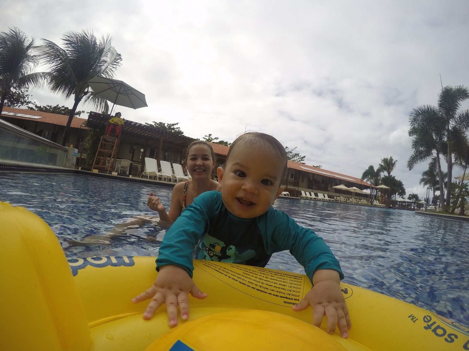 Pedro sorrindo em uma boia amarela na piscina, em Maceió